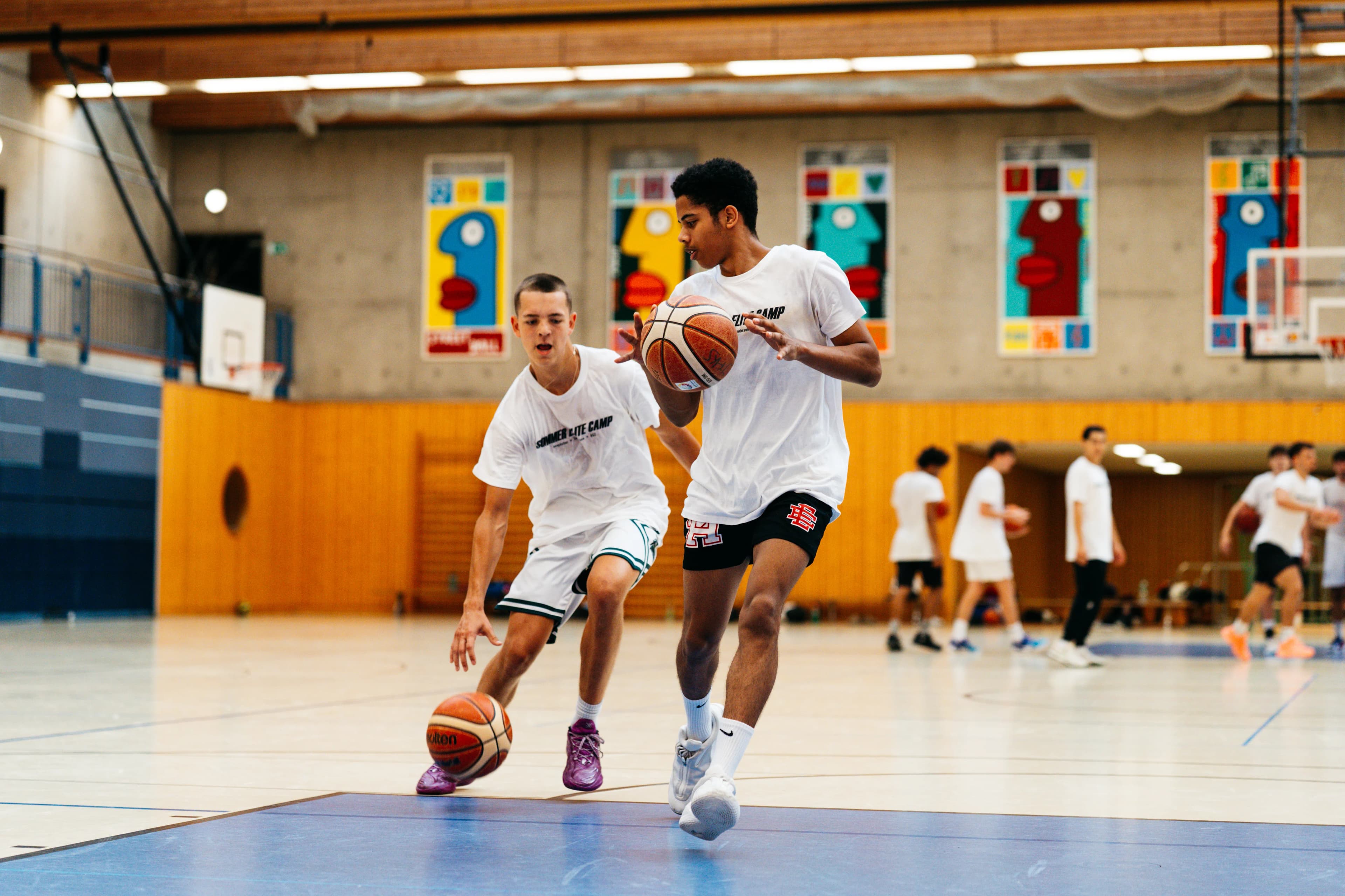 Two players dribbling side by side in a Berlin gym at the Sommer Elite Camp