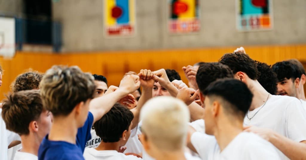 Young players in a huddle, hands together, at a basketball camp